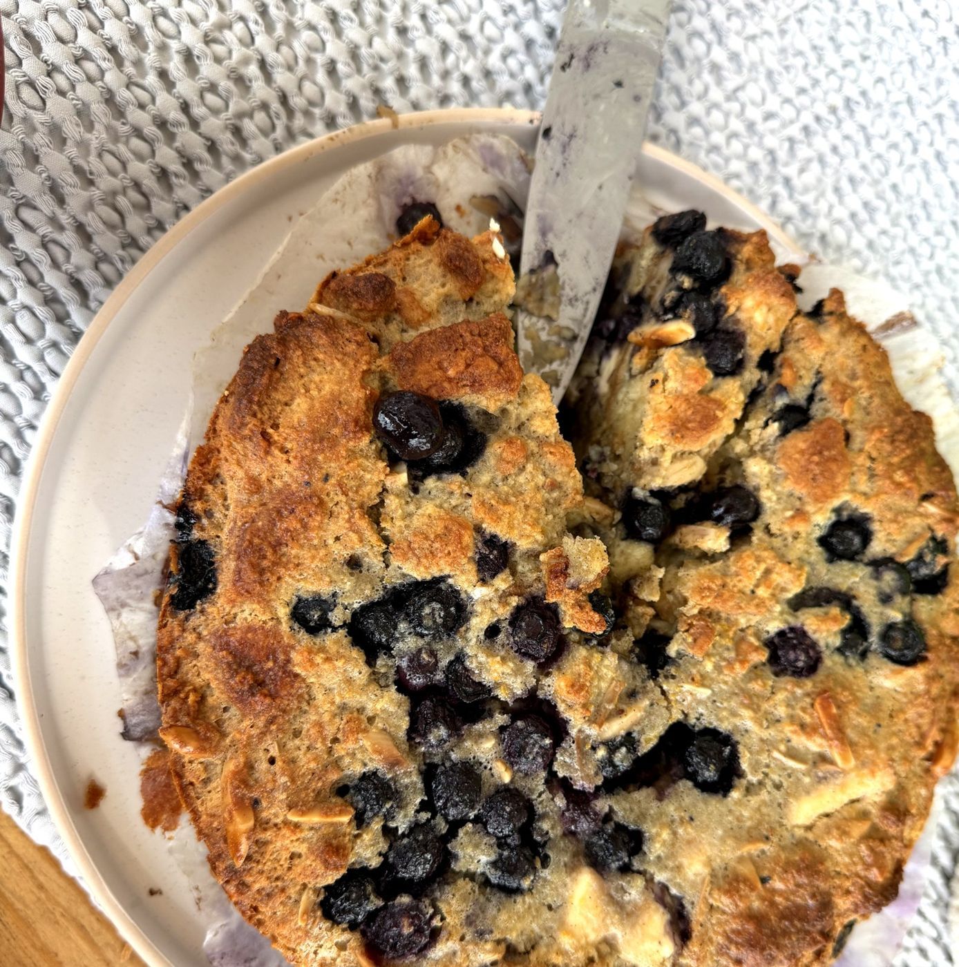 Golden blueberry tea biscuit pudding in a round dish, knife resting on top, blueberries scattered across the puffed top