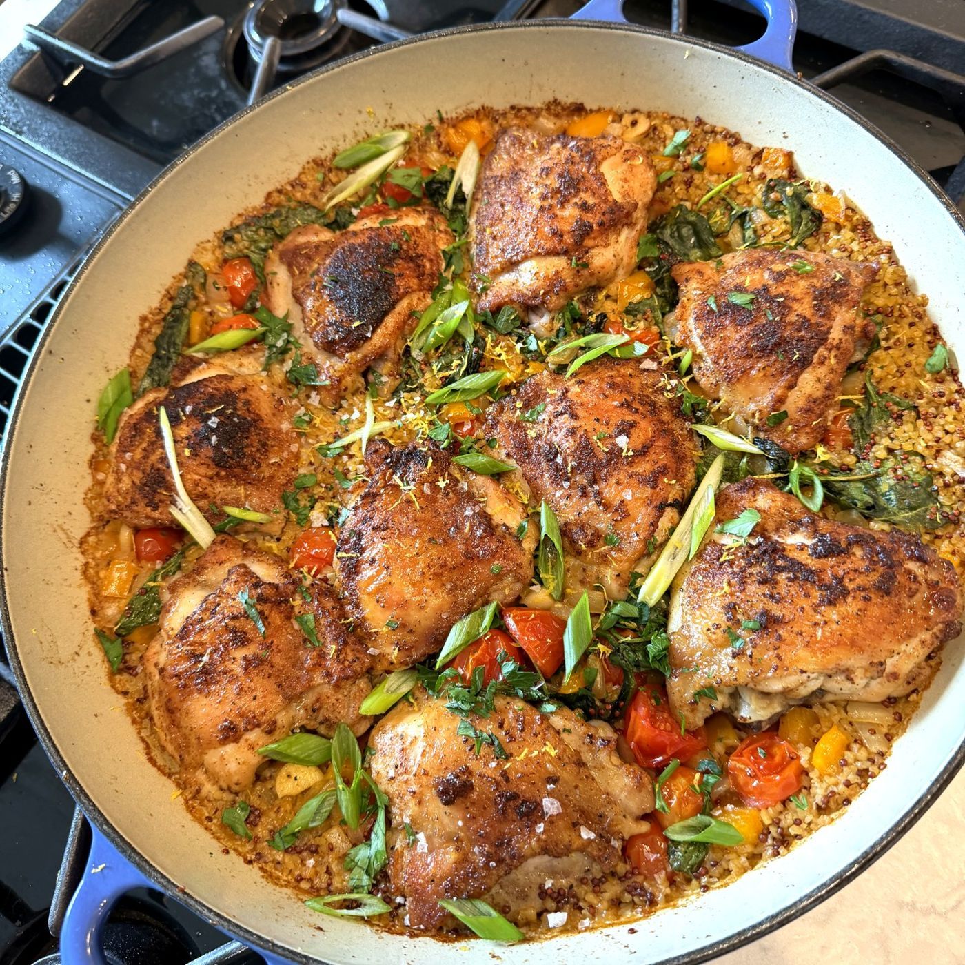 Crisp-skinned cast-iron chicken thighs over a quinoa-bulgur pilaf with cherry tomatoes, peppers, scallions, and herbs