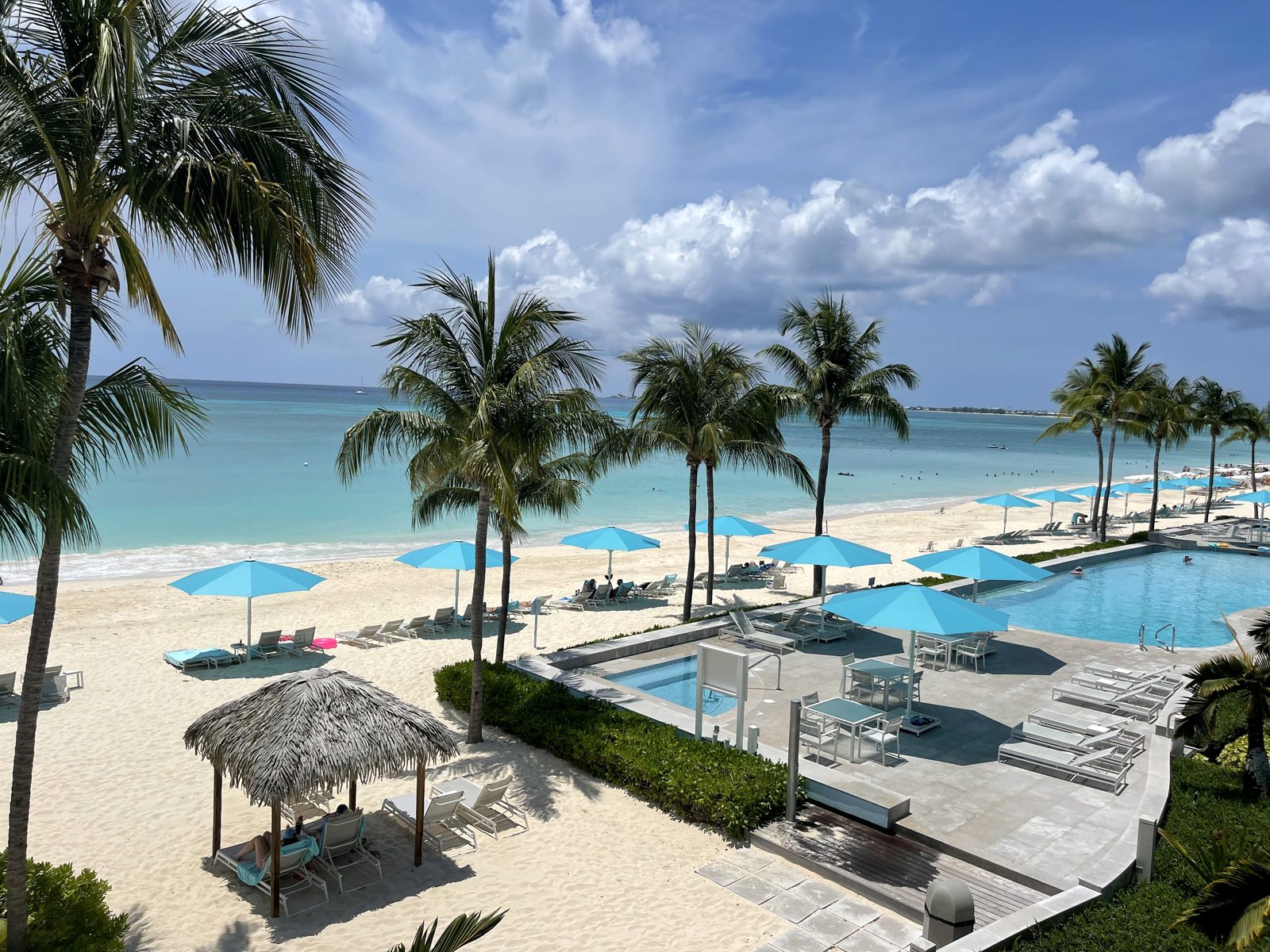 Palm trees, blue umbrellas and a pool above the white sand and turquoise water of Seven Mile Beach