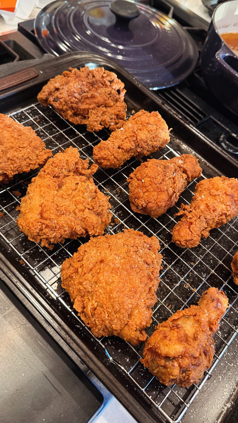 A tray of golden, craggy fried chicken thighs and drumsticks cooling on a wire rack