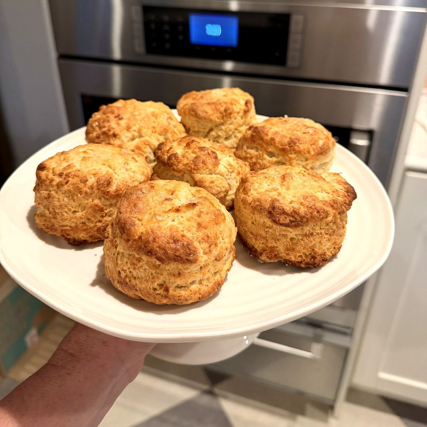 A plate of tall, golden ricotta biscuits held up in front of an oven