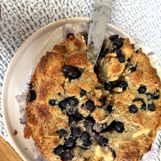 Golden blueberry tea biscuit pudding in a round dish, knife resting on top, blueberries scattered across the puffed top