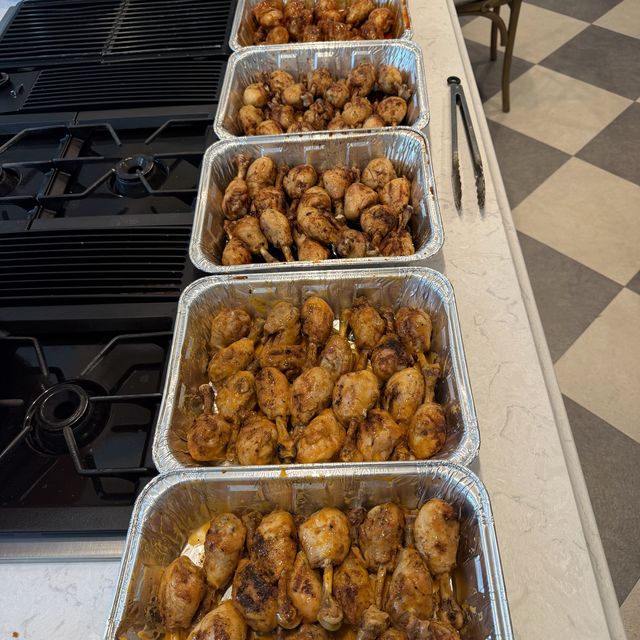 Six foil trays of grilled, spiced chicken lined up along a kitchen counter