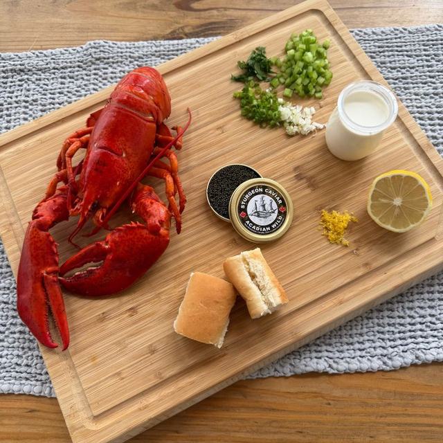 Lobster, caviar, lemon and brioche rolls laid out on a wooden board