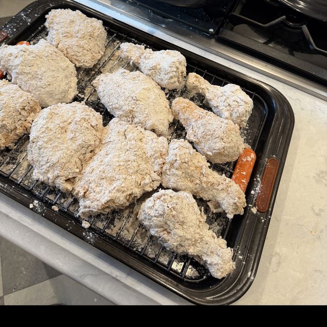 Chicken pieces dredged in seasoned flour on a rack, next to a Dutch oven of hot oil