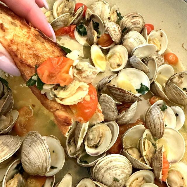 Toasted baguette loaded with clams and a blistered cherry tomato, dunked into a Dutch oven of garlic clams