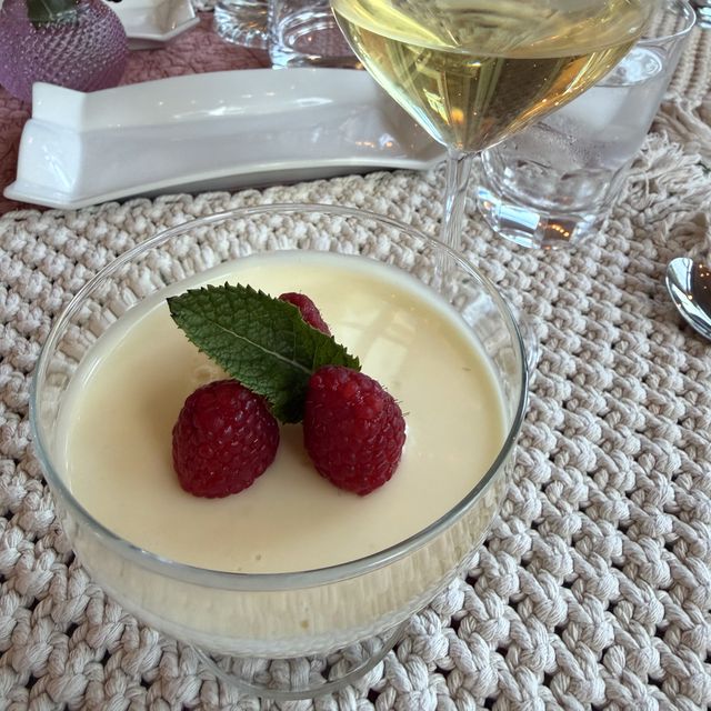 Lemon posset with raspberries and mint, a glass of white wine behind it