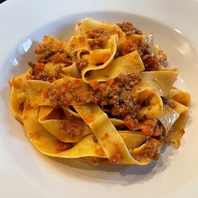 Pappardelle tossed in a rich bolognese in a white bowl
