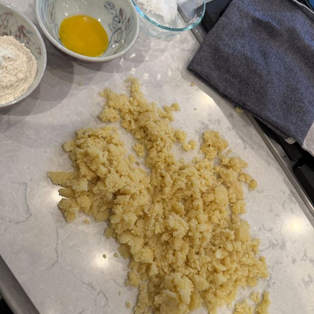 Riced potato on the counter beside bowls of flour, egg yolk and salt