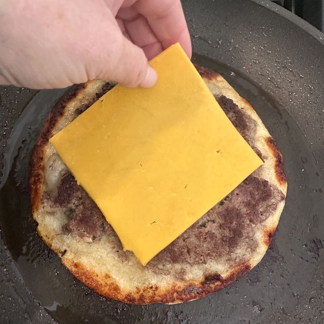 A slice of cheddar going onto a flipped, crisp smash burger taco in the pan