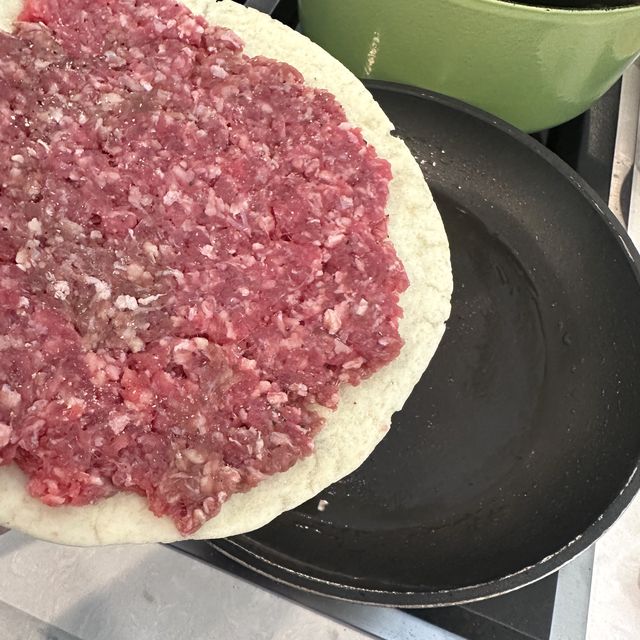 Beef pressed thin onto a flour tortilla for smash burger tacos
